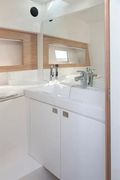 Modern boat bathroom featuring a sleek sink, chrome taps, wooden accents, and a large mirror, with natural light from a window.